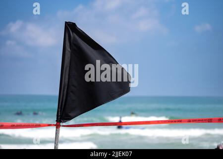 Drapeau noir avec un ruban rouge sur la rive de la mer avertissement sur le courant dangereux et les vagues ou l'invasion de méduses. Banque D'Images