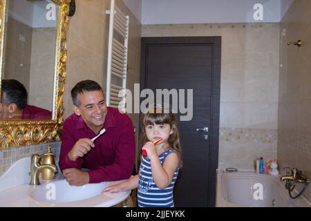 Image d'un jeune père souriant avec une brosse à dents dans sa main, qui apprend à sa fille à se brosser les dents dans la salle de bains. Référence aux soins buccaux Banque D'Images