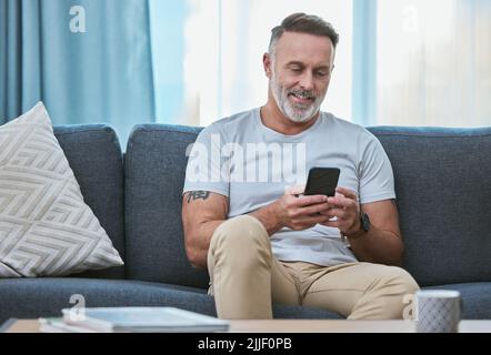 Un homme mûr se détendant à la maison tout en utilisant son smartphone. Banque D'Images