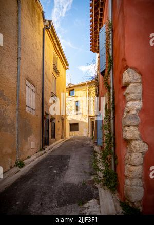 Vieille rue du village de Gruissan, dans le sud de la France, avec des murs de couleur beige et rose ainsi que des volets bleus, pris sur un hiver ensoleillé tard après Banque D'Images
