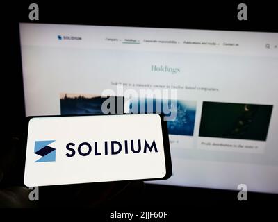 Personne tenant un téléphone portable avec le logo de la société d'investissement finlandaise Solidium Oy sur l'écran en face de la page Web d'affaires. Mise au point sur l'affichage du téléphone. Banque D'Images