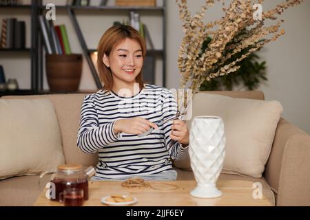 Jeune femme asiatique positive coupant et organisant des fleurs séchées dans un bouquet Banque D'Images