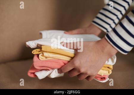 Mains de la femme mettant des t-shirts rangés pliés sur le canapé Banque D'Images