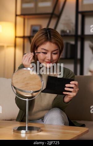 Souriante jeune femme asiatique se maquillant avant le travail ou la date romantique Banque D'Images