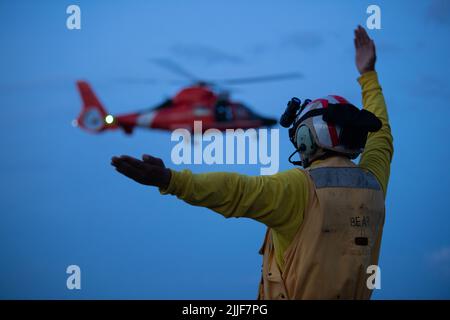 Officier de la garde côtière américaine classe 1st Ricardo Aguilar, technicien en électronique à bord de l'ours de garde côtière (WMEC 901), dirige un dauphin MH-65 de la Garde côtière, un atout de l'escadron tactique d'interception d'hélicoptères de la Garde côtière (HITRON), jusqu'au pont de vol du navire, Atlantic Ocean 13 juillet 2022. Aguilar était l'officier de signalisation d'atterrissage sur le pont. (É.-U. Photo de la Garde côtière par Petty Officer 3rd classe Matthew Abban) Banque D'Images