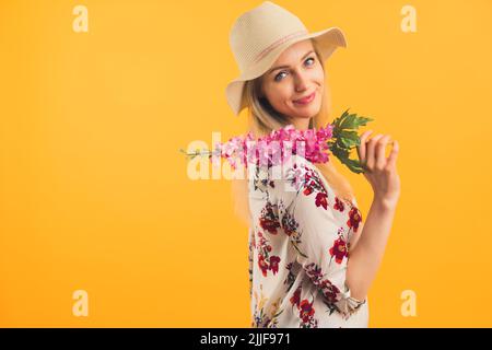 Une fille blonde portant un chapeau tenant une fleur regardant la caméra sur fond orange . Photo de haute qualité Banque D'Images