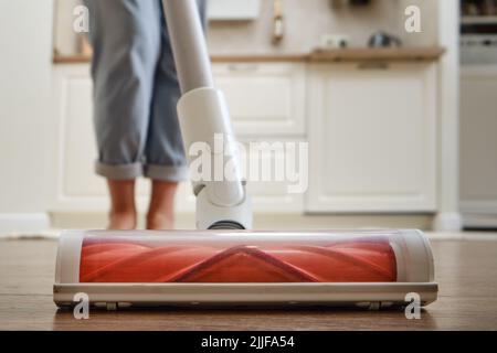 Femme avec un aspirateur portable sans fil dans la cuisine. Nettoie le sol d'un appartement avec un aspirateur avec une batterie Banque D'Images