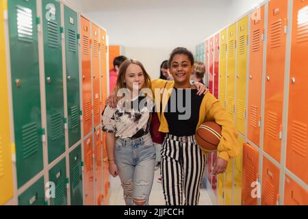 Les jeunes élèves du secondaire se rencontrent et saluent à proximité d'un casier dans le couloir du campus qui parle et marche ensemble. Banque D'Images