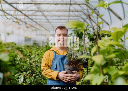 Jeune employé heureux avec le syndrome de Down travaillant dans le centre de jardin, prenant soin des fleurs. Banque D'Images