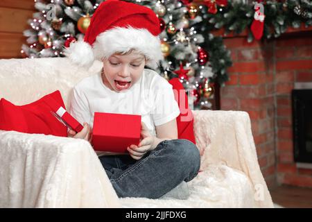 Joyeux Noël aux enfants. Émotions d'un enfant. Joyeux enfant surpris garçon dans le chapeau du Père Noël a ouvert une boîte de Noël avec un cadeau du Père Noël près du Christ Banque D'Images