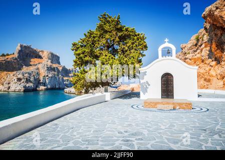 Rhodes, Grèce. Baie de Saint Paul avec chapelle blanche. Paysage de la mer Égée avec l'ancienne ville de Lindos et les ruines rocheuses de l'Acropole. Banque D'Images