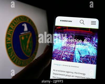 Personne tenant un smartphone avec le site Web du Département de l'énergie des États-Unis (DOE) sur l'écran devant le sceau. Concentrez-vous sur le centre de l'écran du téléphone. Banque D'Images