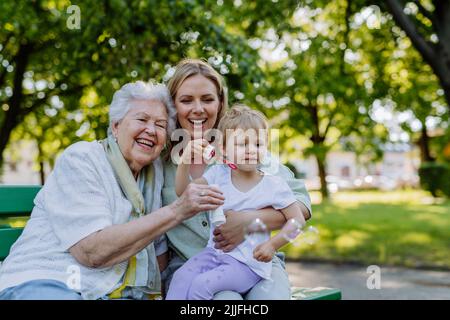 Femme souriante heureuse avec grand-mère senior et petite fille soufflant des bulles de savon au parc, famille, génération et concept de personnes. Banque D'Images