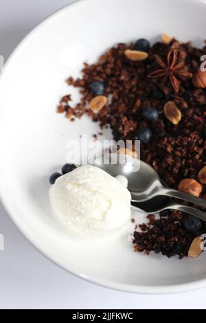 Une cuillère de glace à la vanille accompagnée d'un dessert de granola aux myrtilles et de noix. Banque D'Images