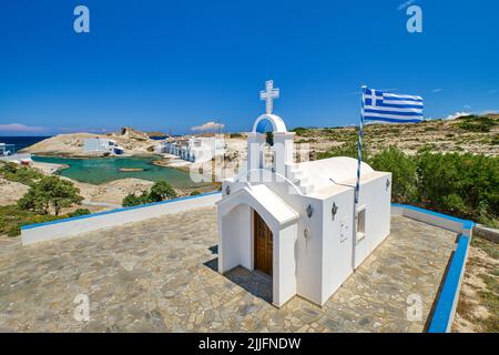 Chapelle ou église orthodoxe grecque blanche, croix blanche et drapeau national grec sur la colline le jour d'été ensoleillé. Paysage de l'île grecque. Milos, Grèce Banque D'Images