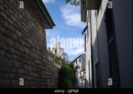 Rue étroite avec vue sur l'église San Lorenzo à Porto Venere, Ligurie, Italie. Passage entre le mur de pierre et les maisons italiennes avec des volets sur les fenêtres. Banque D'Images