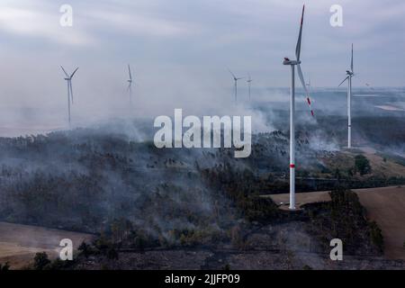 Falkenberg, Allemagne. 26th juillet 2022. Des nuages de fumée se délellent au-dessus d'une zone forestière au cours d'un incendie de forêt entre des éoliennes en début de matinée. Les pompiers de Brandebourg continuent de lutter contre un grand incendie de forêt dans le district d'Elbe-Elster. Depuis lundi (25,07), il brûle sur une superficie d'environ 800 hectares. Les premiers résidents ont dû quitter leur maison. (Vue aérienne avec drone) Credit: Jan Woitas/dpa/Alamy Live News Banque D'Images
