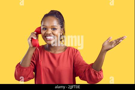 Une femme joyeuse entend de bonnes nouvelles tout en parlant sur un téléphone rétro fixe sur fond jaune. Banque D'Images