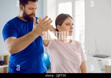 Un physiothérapeute masculin sérieux examine le bras blessé d'une patiente en clinique médicale. Banque D'Images