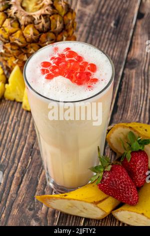 Smoothie à la banane, aux fraises et à l'ananas sur une table en bois et thé moussant ou boules de thé boba Banque D'Images