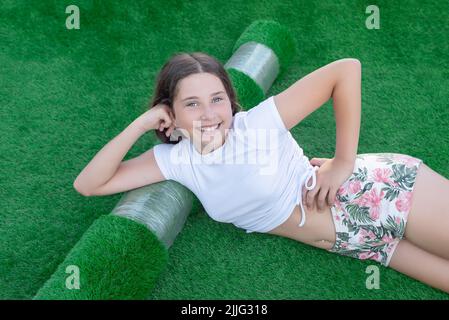 Jeune fille caucasienne souriante couché sur un nouveau rouleau de gazon artificiel. Herbe artificielle agréable prête à pondre Banque D'Images