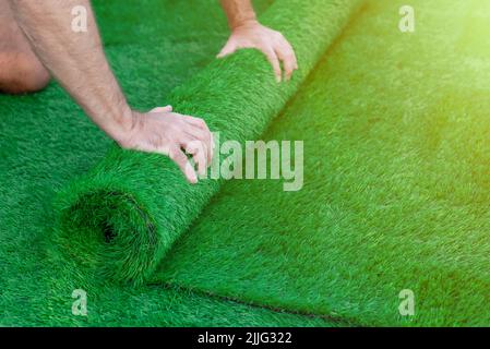 Accent sélectif sur les mains d'un homme qui déroulent un rouleau de gazon artificiel. Pose facile d'herbe verte artificielle Banque D'Images