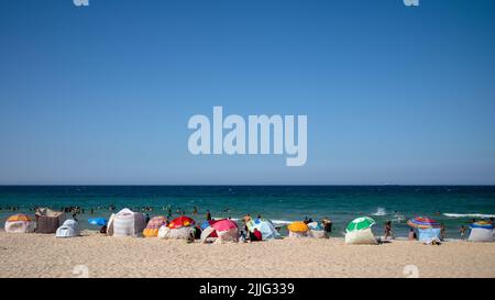 Les gens jouent dans la mer ou s'assoient dans leurs abris en profitant de la plage de Bou Jaafar à Sousse, en Tunisie. Banque D'Images