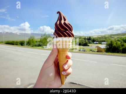 Main tenant savoureux de la crème glacée locale douce islandaise à la vanille trempée dans le chocolat chaud, la nature islandaise sur fond. Banque D'Images