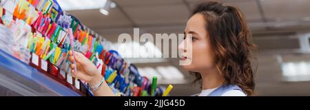 jeune femme brune choisissant le stylo sur le rack dans la papeterie magasin, bannière Banque D'Images