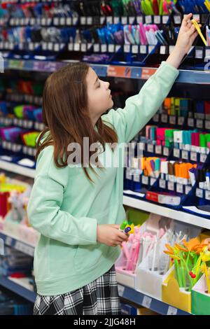 fille choisissant les fournitures scolaires sur le rack dans le magasin de papeterie Banque D'Images