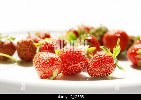 Les fraises fraîches avec des feuilles sont éparpillées sur la plaque blanche au fond du backgroung blanc isolé. Fraises juteuses pour vegan, vegeteri Banque D'Images