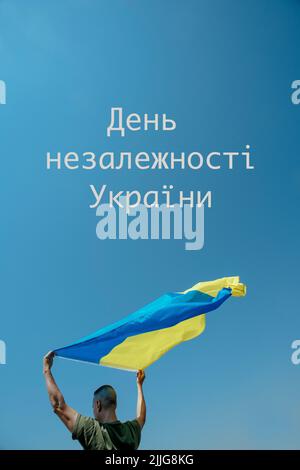 le texte jour de l'indépendance de l'ukraine écrit en ukrainien et un homme agitant le drapeau ukrainien sur le ciel au-dessus de sa tête, dans un jour ensoleillé Banque D'Images