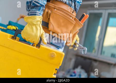 Gros plan de la boîte à outils jaune portée par un travailleur de la construction portant une ceinture à outils en cuir et des gants de protection. Site de construction en arrière-plan. Banque D'Images