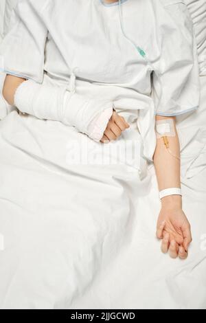 Injection verticale de haut en bas d'une patiente méconnaissable dont le bras est cassé en fonte et qui reçoit des médicaments ou des liquides nutritifs par voie intraveineuse Banque D'Images