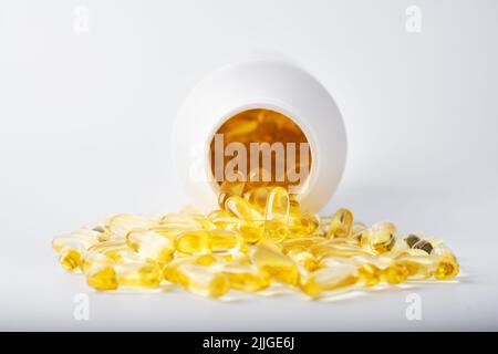 Capsules d'huile de poisson jaune dans une coquille de gelée près du pot blanc. Vitamines et compléments alimentaires. Concept de santé Banque D'Images