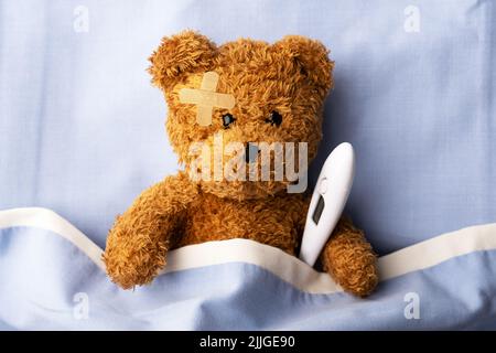 Ours en peluche malade sur le lit d'hôpital avec thermomètre et plaque de plâtre sur la tête. Concept de médecine pédiatrique et pédiatrique Banque D'Images