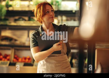 Propriétaire d'une épicerie prenant des stocks à l'aide d'une tablette numérique dans son magasin. Jeune femme entrepreneur à la gestion de sa petite entreprise en utilisant la technologie sans fil Banque D'Images