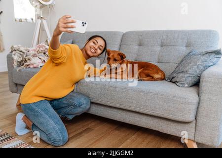 Une jeune femme hispanique prend une photo de selfie avec son chien au téléphone portable à la maison Banque D'Images