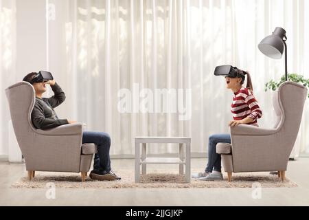 Un jeune homme et une jeune femme assis dans des fauteuils à l'aide de casques de réalité virtuelle à la maison Banque D'Images