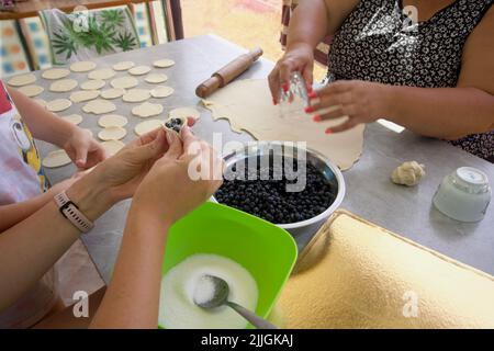 Une femme prépare de la pâte pour les boulettes de bleuets. Une autre femme met la farce dans la pâte. Banque D'Images