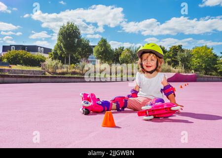 Petite fille apprendre à utiliser des rouleaux, s'asseoir souriant au skate Park Banque D'Images