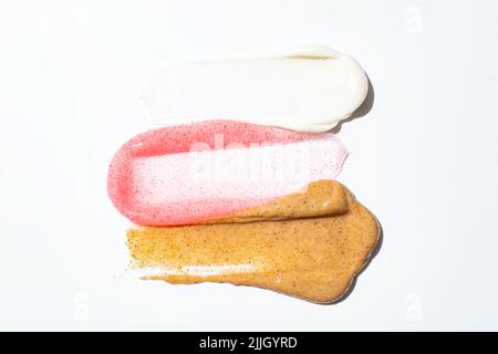 Gommage du visage texture crémeuse. Blanc, rose et brun naturel savon exfoliation à frottis isolé sur blanc. Exemple de masque facial. Soin spa Banque D'Images