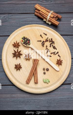 Séchez les épices sur une planche ronde en bois. Toutes les épices dans une cuillère, anis étoilé et clous de girofle. Les bâtonnets de cannelle sont noués dans un paquet. Pose à plat. Arrière-plan en bois sombre. Banque D'Images