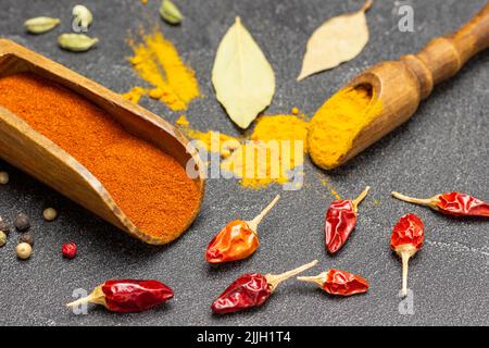 Poivre moulu et curcuma dans des pelles en bois. Des gousses de poivre rouge sec sur la table. Vue de dessus. Arrière-plan noir Banque D'Images