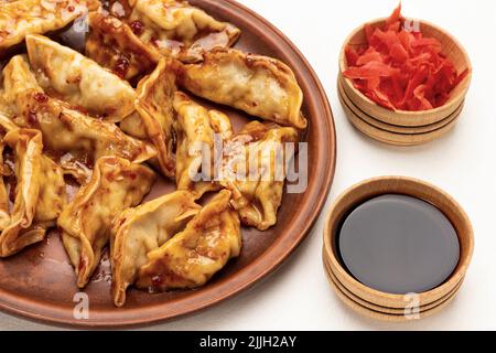 Boulettes de gedza bouillies en sauce sur plaque de céramique. Sauce au gingembre et au soja marinés dans des bols. Vue de dessus. Arrière-plan blanc Banque D'Images