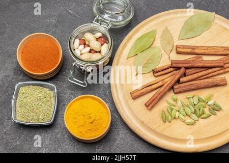 Bâtonnets de cannelle, cardamome et feuille de Laurier à bord. Écrous dans un pot en verre. Curcuma moulu et paprika dans des bols. Pose à plat. Arrière-plan noir Banque D'Images