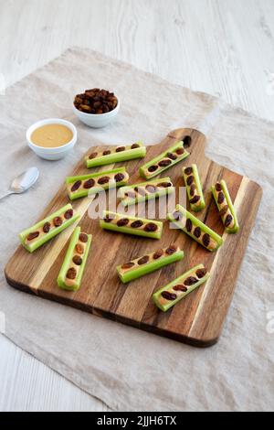 Fourmis maison sur une bûche de céleri, beurre d'arachide et raisins secs sur une planche de bois, vue latérale. Banque D'Images