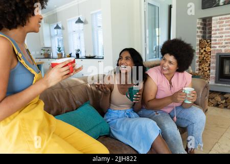 Une jeune femme biraciale parle avec des amies gaies en riant tout en étant assise sur un canapé à la maison Banque D'Images