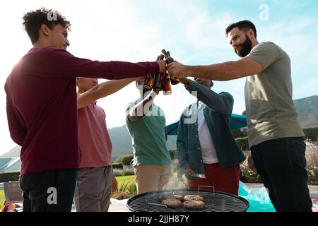 Vue à angle bas des amis multiraciaux qui toastent des bouteilles de bière tout en s'amusant à la fête au barbecue Banque D'Images