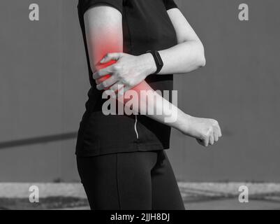 Sportswoman souffrant de douleurs au coude avec point rouge. Utilisation excessive, formation intensive conséquences. Problèmes de santé causés par les blessures sportives concept. Noir et blanc. Photo de haute qualité Banque D'Images